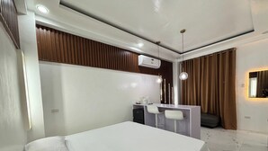 A modern hotel room with a bed, a desk with two chairs, a mirror, and a wall-mounted air conditioner. - Alejandro'S Suites & Venue (Valencia)
