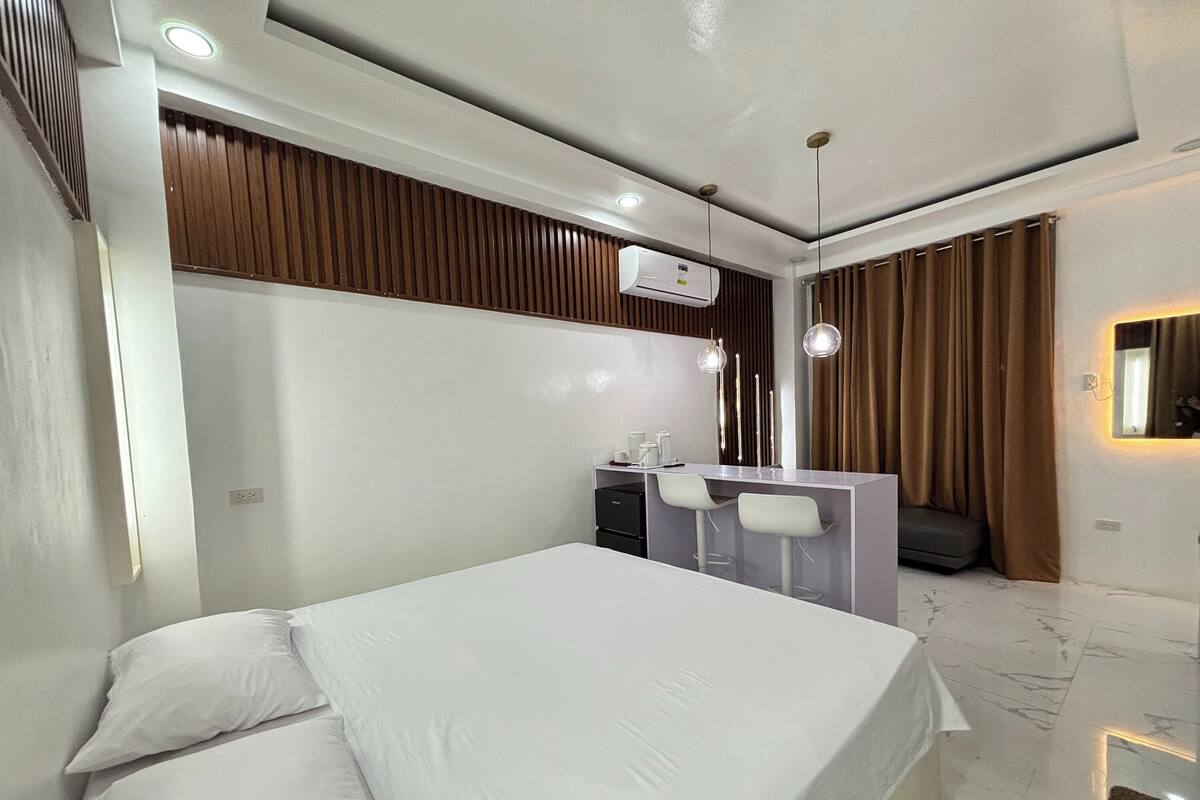 Una habitación de hotel moderna con una cama, un escritorio con dos sillas, un espejo y un aire acondicionado instalado en la pared.