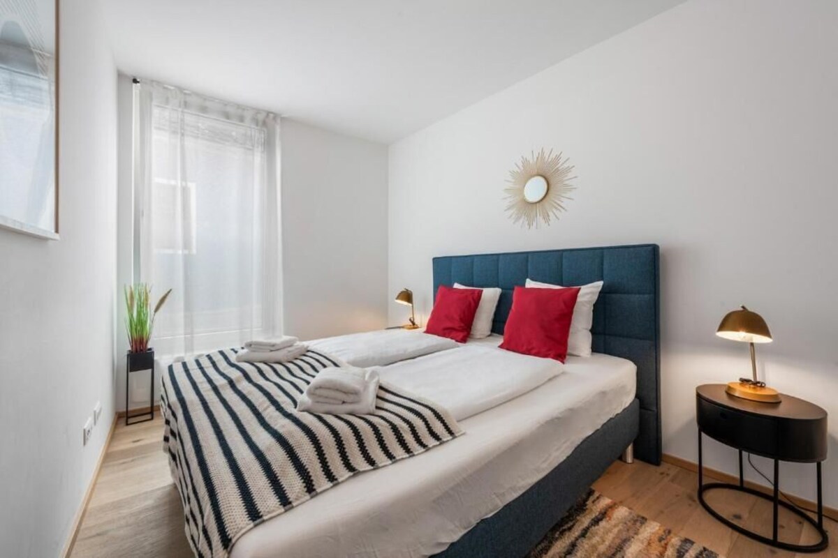 A modern hotel room with a large bed, a blue headboard, and a sunburst wall decoration.