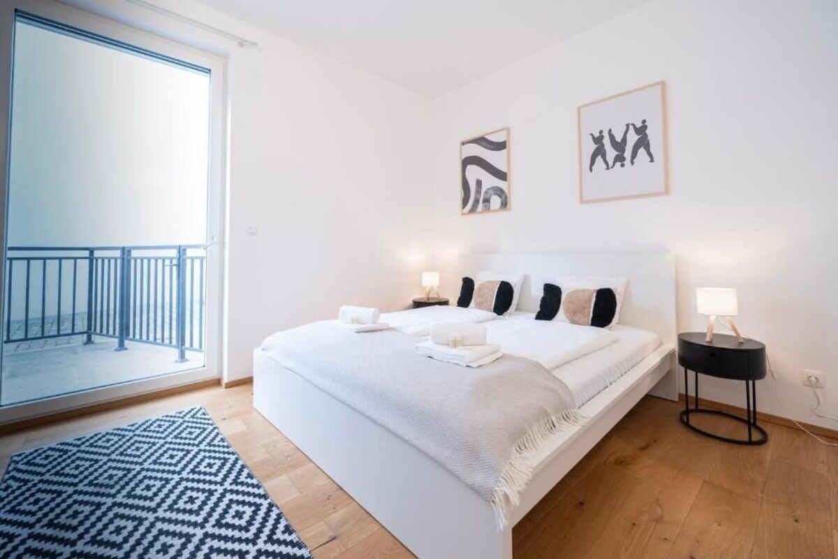 A modern bedroom with a large bed, a balcony, and two framed artworks on the wall.