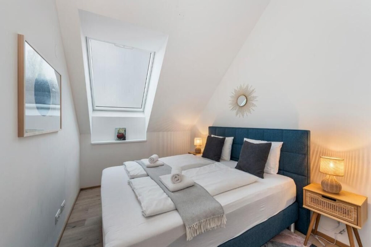 A bedroom with a large bed, a skylight, a bedside lamp, and a wall-mounted clock.