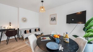 En moderne stue med et rundt spisebord, en sofa og et tv ophængt på væggen.