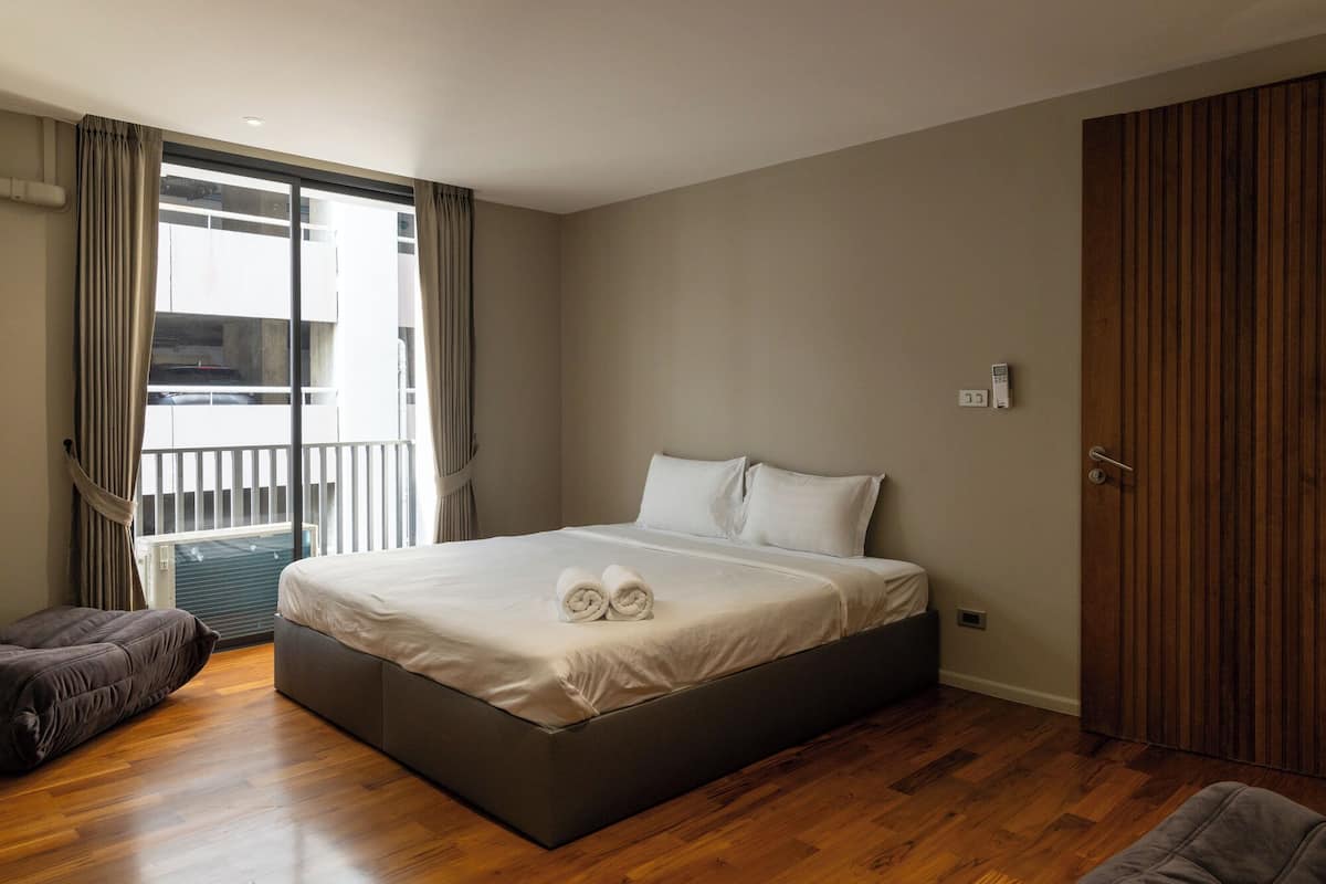 A modern bedroom with a large bed, a wooden floor, a balcony with curtains, and a wardrobe.