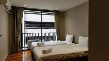 A hotel room with two beds, an air conditioning unit, a window with curtains, and a view of a parking garage.