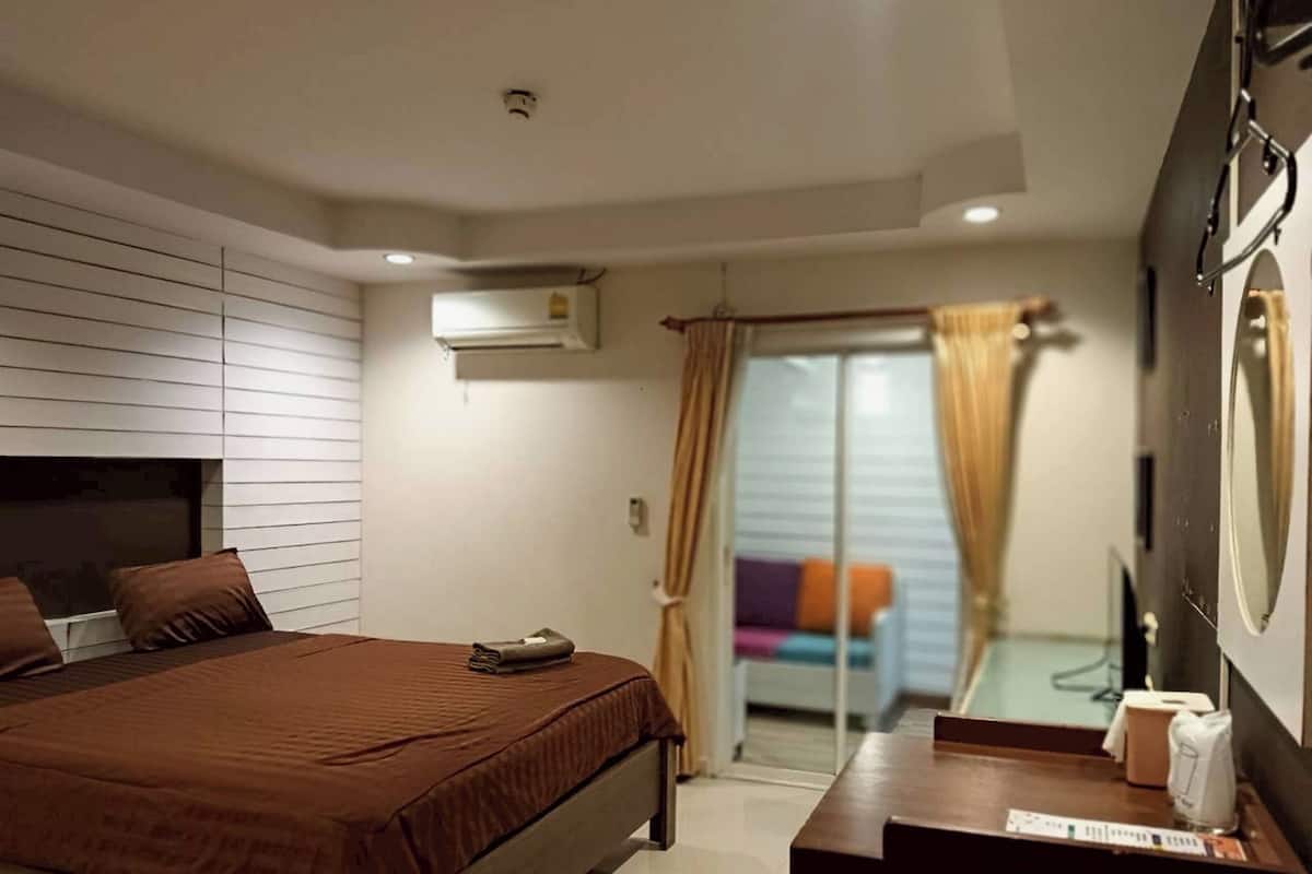 Un dormitorio con cama, mesita de noche, espejo y puerta corredera de cristal que da a un balcón.