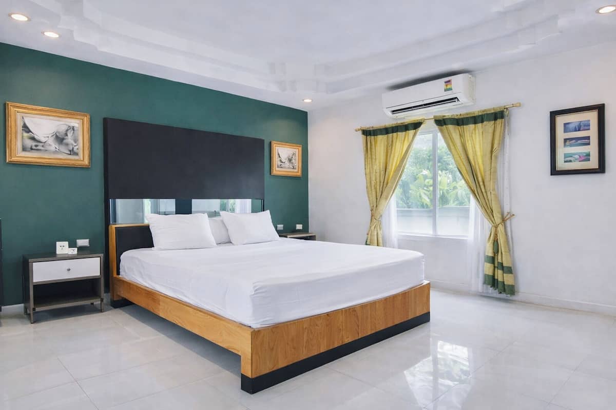 Un dormitorio moderno con una cama grande, una mesita de noche, aire acondicionado de pared y una ventana con cortinas.