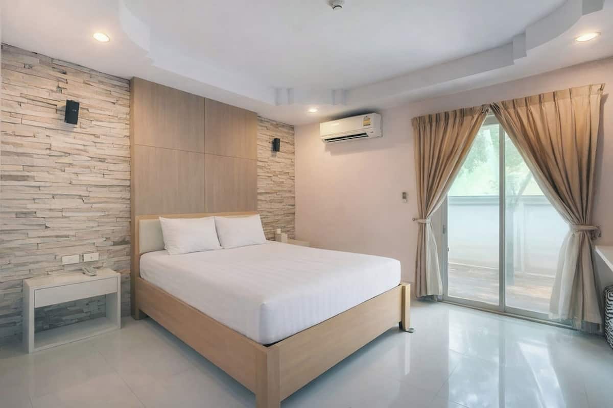Un dormitorio moderno con cama de madera, pared de piedra y un gran ventanal con cortinas.