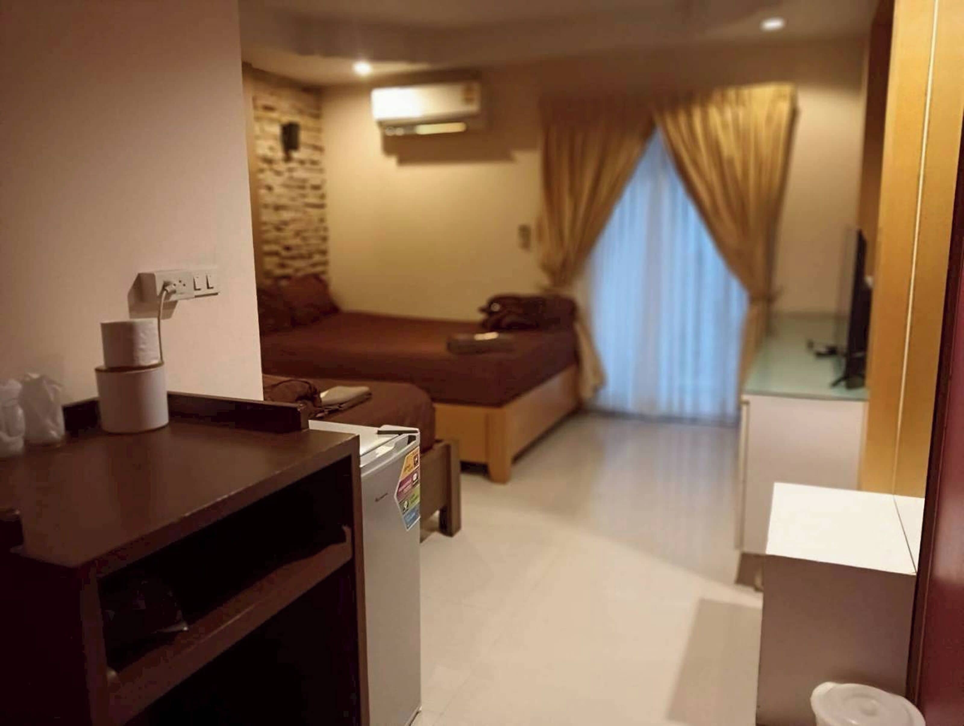 Habitación de hotel con cama, escritorio con computadora, refrigerador pequeño y ventana con cortinas.