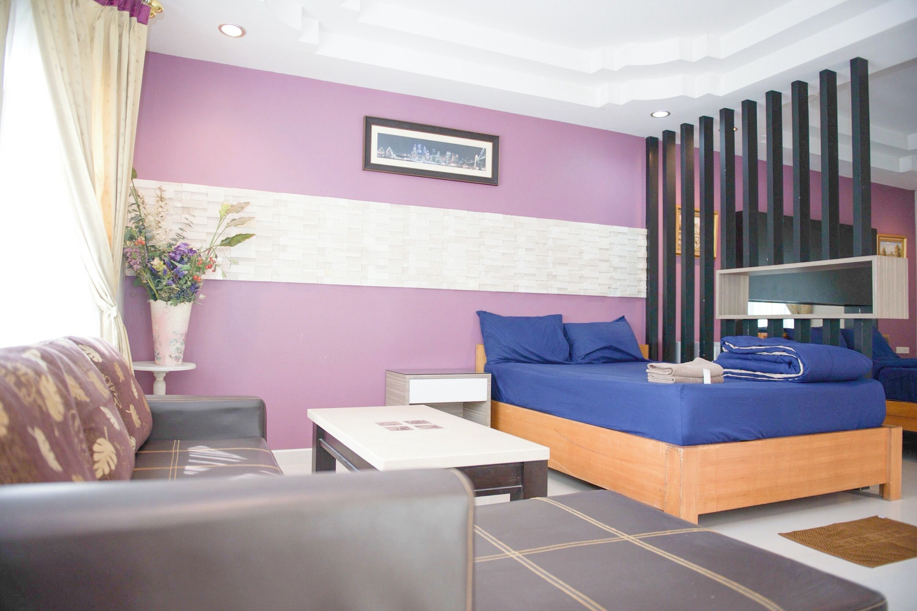 A modern hotel room with a bed, a sofa, a small table, and a decorative plant.