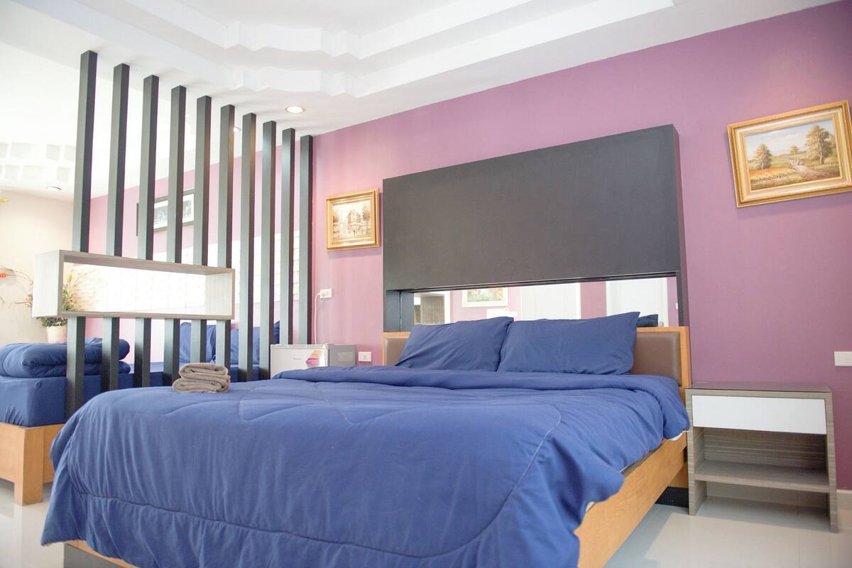 Un dormitorio moderno con una cama grande, una mesita de noche, un televisor montado en la pared y un panel decorativo.