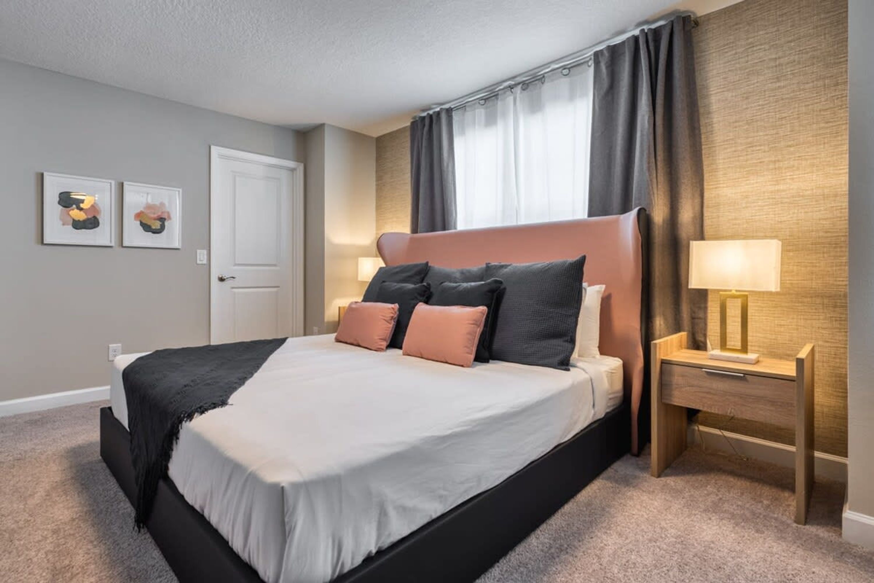 A modern hotel room with a large bed, a nightstand with a lamp, and two framed pictures on the wall.