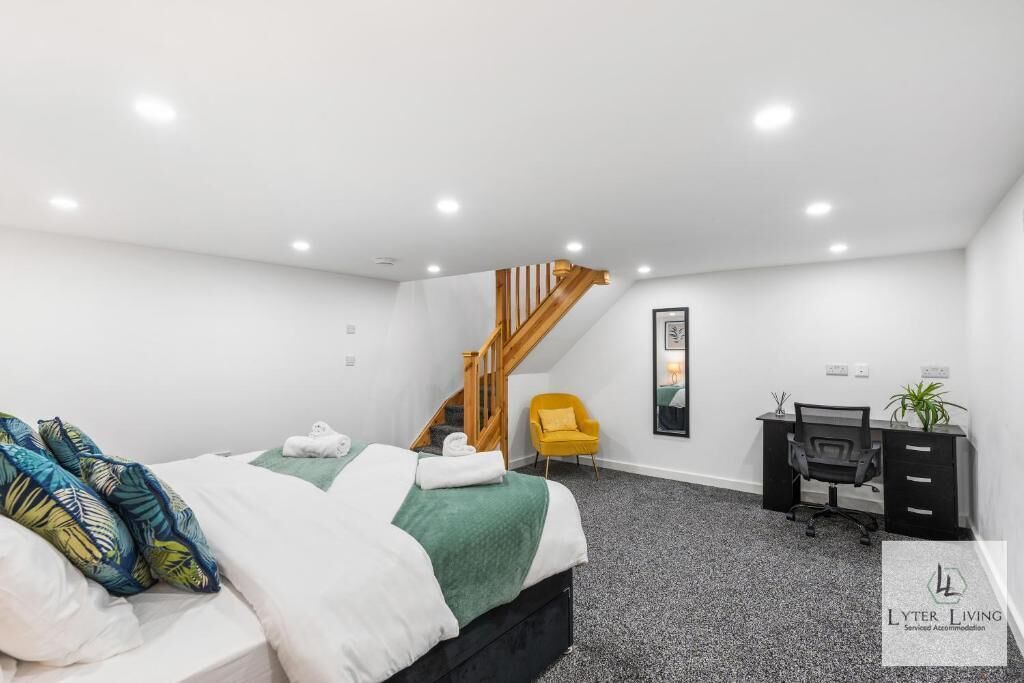 Ein Schlafzimmer mit Bett, Schreibtisch, Stuhl, einer Treppe und einer kleinen Pflanze.