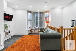 A modern living room with a grey sofa, orange rug, and a TV mounted on the wall.