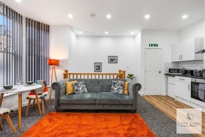 A modern living room with a grey sofa, orange rug, and a dining area with a table and chairs.
