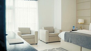 A hotel room with a bed, two armchairs, a bedside table, a lamp, and a window with sheer curtains. - The Mews by Stay Series (Lagos)