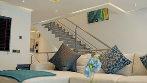 A modern living room with a staircase, a sofa with patterned cushions, and a painting on the wall. - The Mews by Stay Series (Lagos)