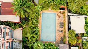 An aerial view of a hotel with a rectangular pool surrounded by lush greenery and palm trees. - The Mews by Stay Series (Lagos)