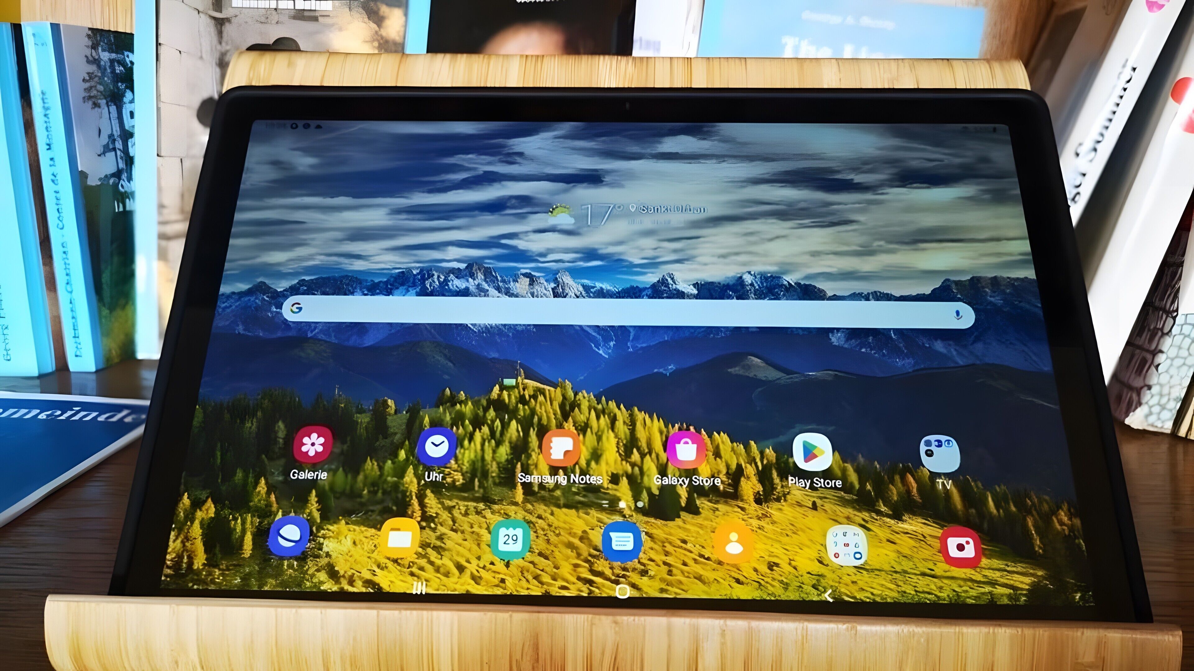 Een tablet op een houten standaard met een berglandschap als achtergrond en app-icoontjes.