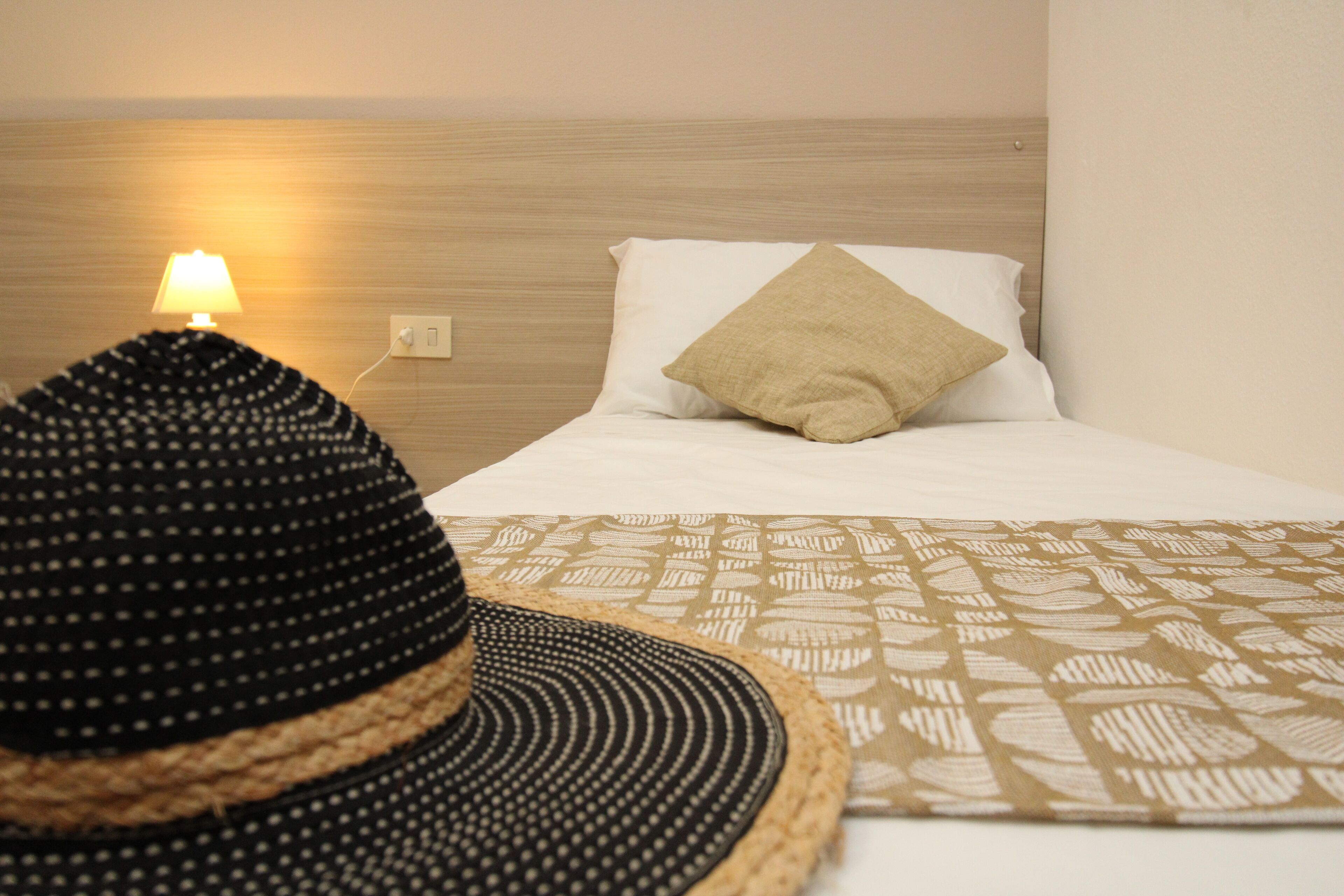 A neatly made bed with a patterned throw, a single pillow, and a lamp on the nightstand.