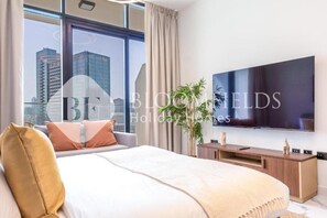 Ein modernes Hotelzimmer mit einem großen Bett, einem Flachbildfernseher, einer Holzkonsole und Blick auf die Stadtlandschaft.