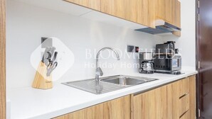 A modern kitchen with wooden cabinets, a stainless steel sink, and a coffee maker. - Bloomfileds Executive Studio Al MA (Abu Dhabi)