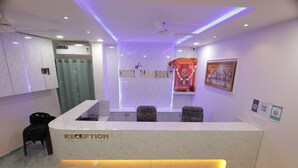 Un espace d’accueil d’hôtel avec un comptoir de réception en marbre, une horloge, un tableau encadré et un objet décoratif fixé au mur.