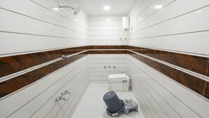 Une salle de bain moderne avec des carreaux blancs, un mur d’accent en marbre, des toilettes, un bidet et une poubelle.