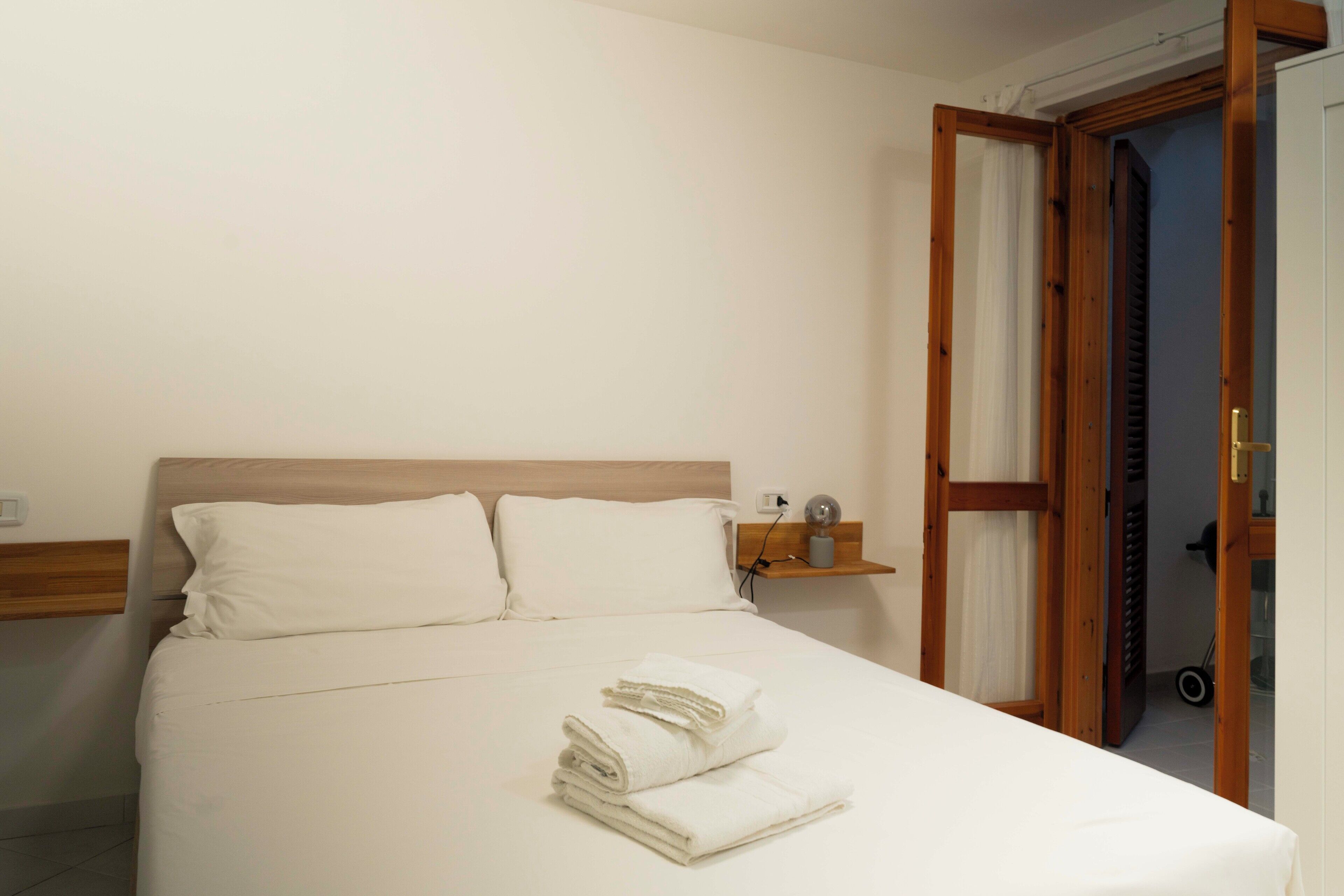 A neatly made bed with white linens and towels, a wooden headboard, and a small bedside table with a lamp.
