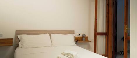 A neatly made bed with white linens and towels, a wooden headboard, and a small bedside table with a lamp.