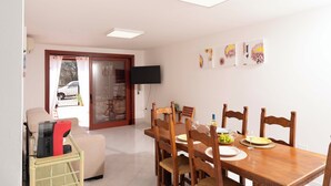 Uma área de refeições com mesa de madeira, cadeiras e uma TV fixada na parede.