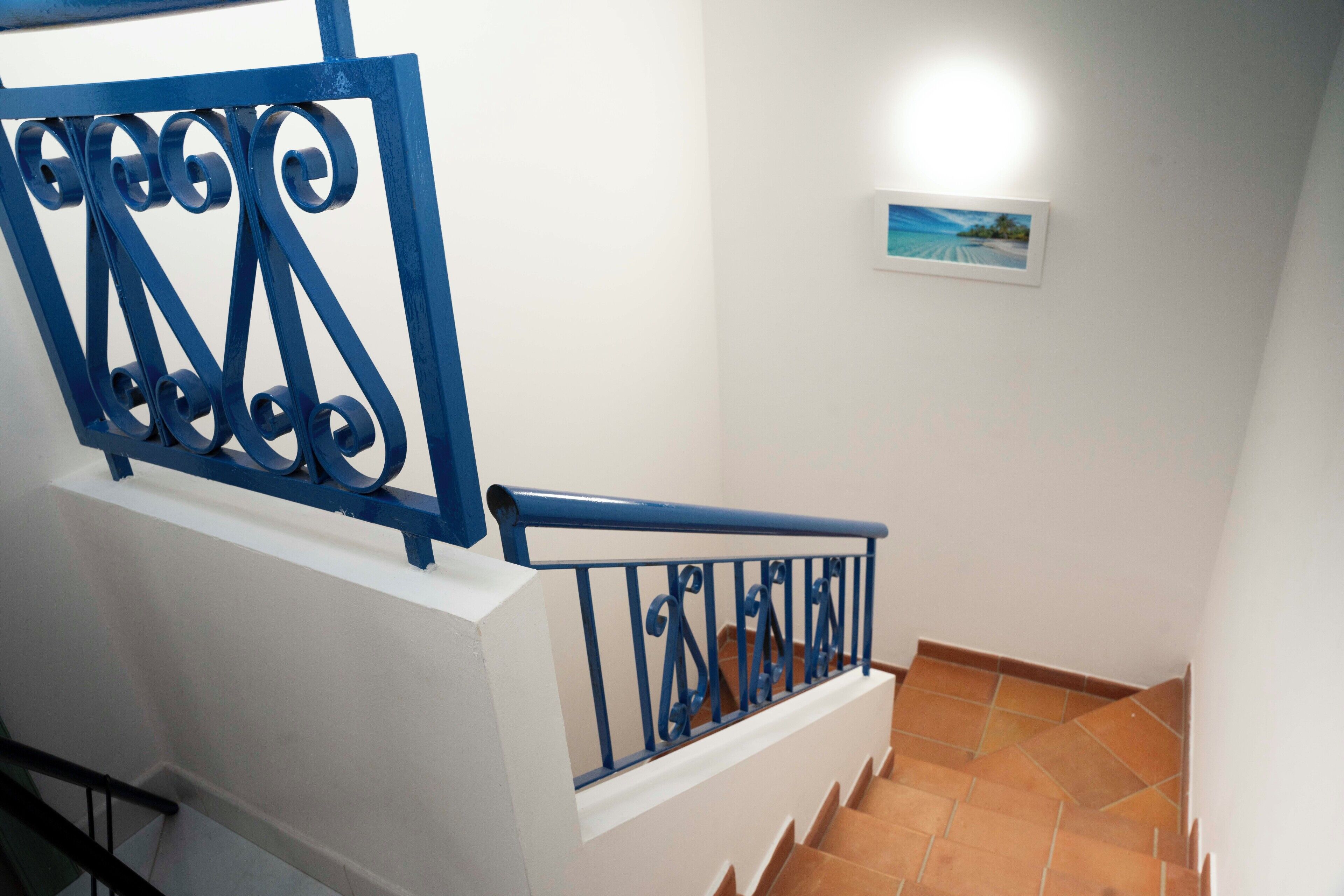 A staircase with blue metal railings and a white wall with a framed picture.