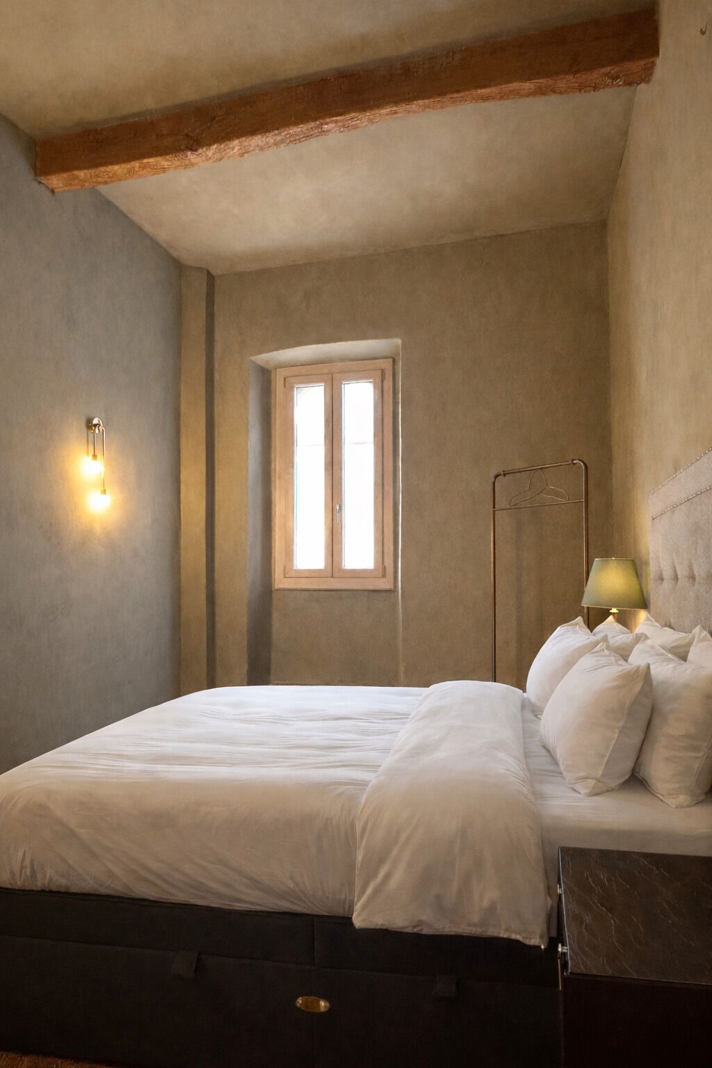 A bedroom with a bed, a nightstand, a lamp, and a window.