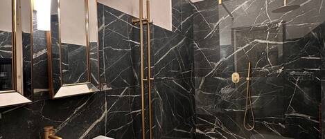A modern bathroom with a white sink, gold fixtures, and black marble walls.