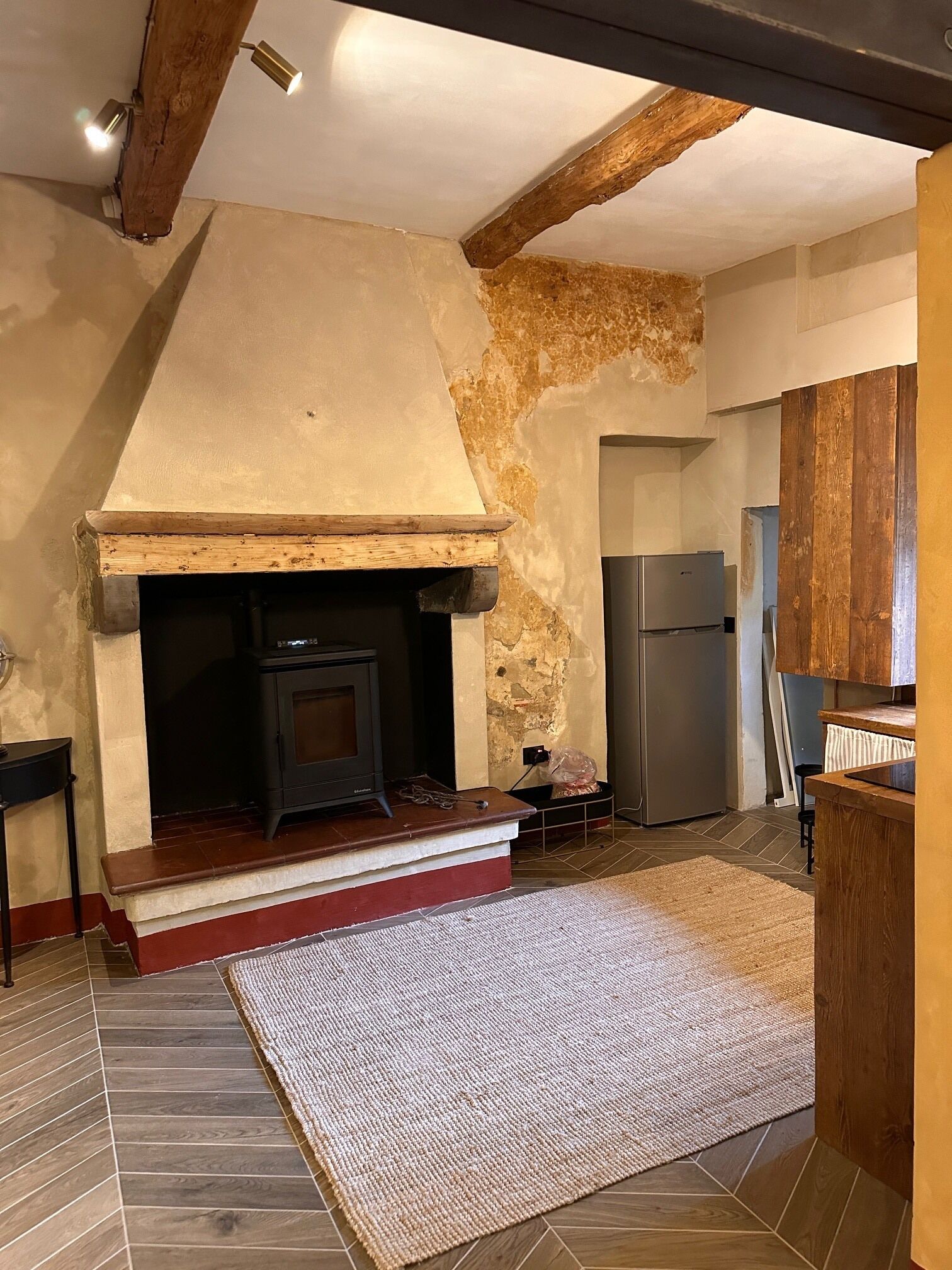 A rustic kitchen with exposed wooden beams, a stone wall, and a built-in wood-burning stove.