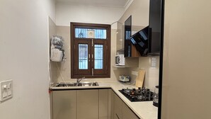 A compact kitchen with a window, a microwave, a stove, and a sink. - Fortune Home Service Apartment 3Bhk J150 (New Delhi)