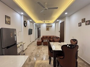 A modern living space with a dining area, a sofa, a TV, and a ceiling fan. - Fortune Home Service Apartment 3Bhk J150 (New Delhi)