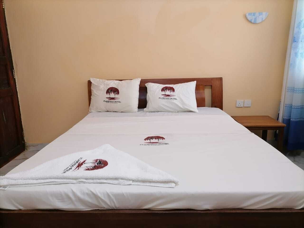 A neatly made bed with white linens and pillows, a wooden headboard, and a small bedside table.