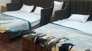 Habitación de hotel con dos camas, cada una con cabecero y almohadas. El suelo es de madera y la pared es lisa.