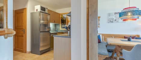 A modern kitchen with a stainless steel refrigerator, wooden cabinets, and a dining area with a wooden table and chairs.