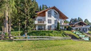 A multi-story building with a sloped roof, surrounded by greenery and trees. - Apartment 'Schladming Planai Mitte' with Mountain View, Private Terrace and Wi-Fi (Schladming)