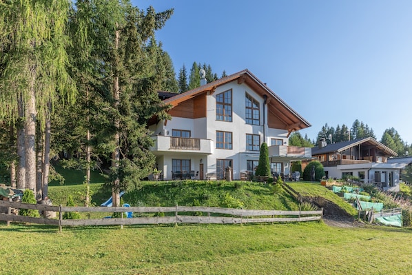 A multi-story building with a sloped roof, surrounded by greenery and trees. - Apartment 'Schladming Planai Mitte' with Mountain View, Private Terrace and Wi-Fi (Schladming)