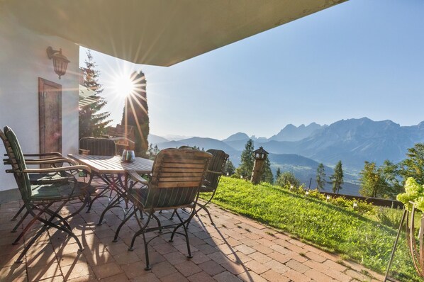 Un patio exterior con mesa y sillas, con vistas a un paisaje montañoso.