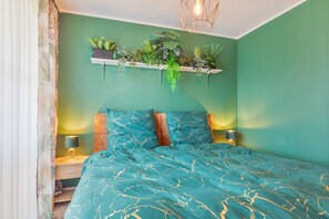 A bedroom with a teal bedspread, a mounted plant shelf, and bedside lamps. - Apartment 'Schladming Planai Mitte' with Mountain View, Private Terrace and Wi-Fi (Schladming)