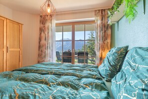 A bedroom with a bed, curtains, a window with a mountain view, and a hanging plant. - Apartment 'Schladming Planai Mitte' with Mountain View, Private Terrace and Wi-Fi (Schladming)