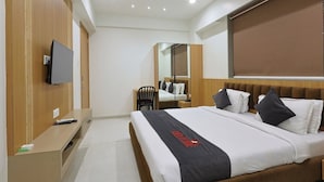 A modern hotel room with a bed, a desk, a chair, a TV, and a mirror. - Hotel Vivanta Inn (Veraval)