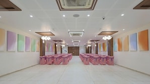 A spacious hall with rows of pink chairs, ceiling lights, and wall-mounted air conditioning units. - Hotel Vivanta Inn (Veraval)