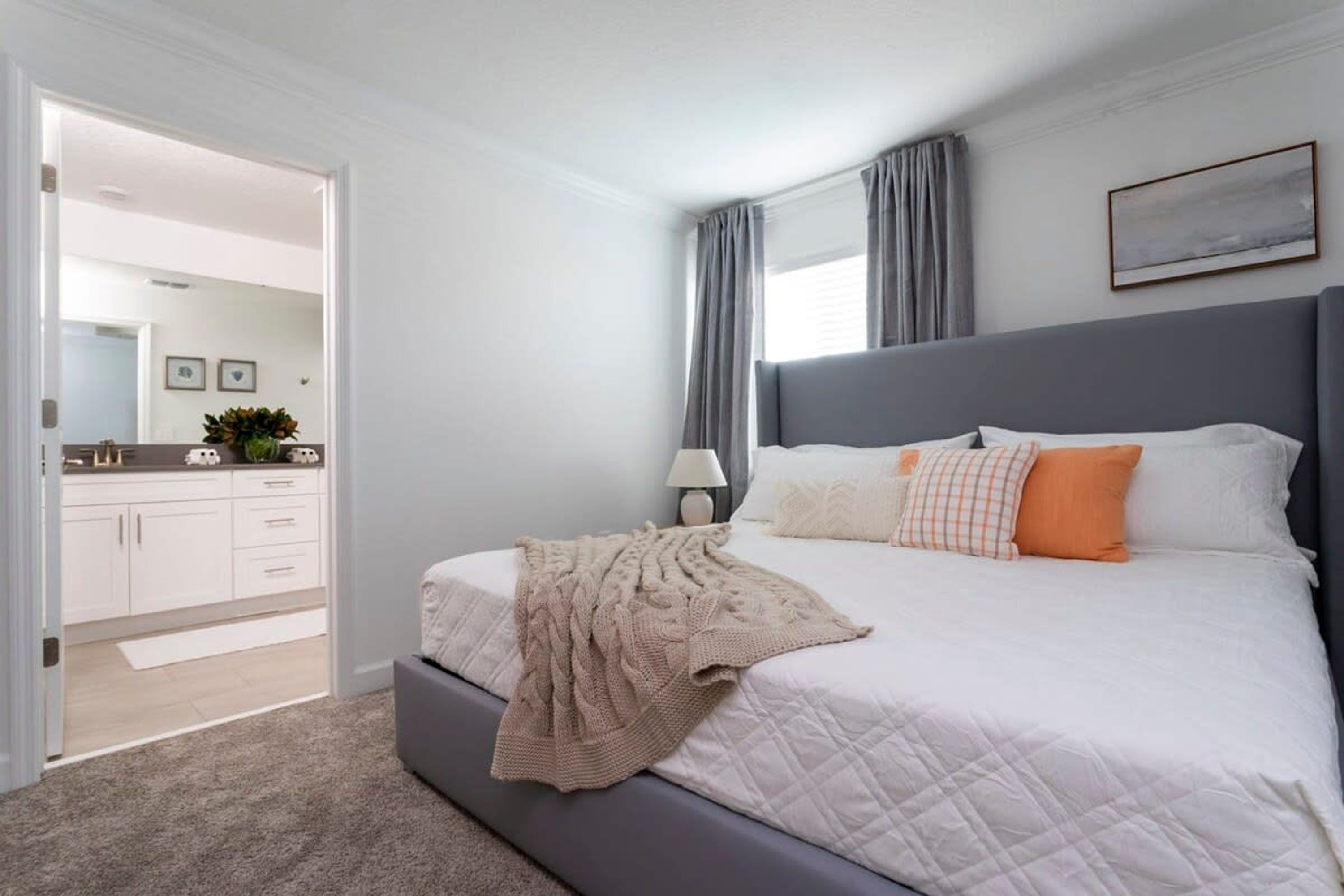 A modern bedroom with a large bed, a bedside table, a lamp, and a view of the hallway.