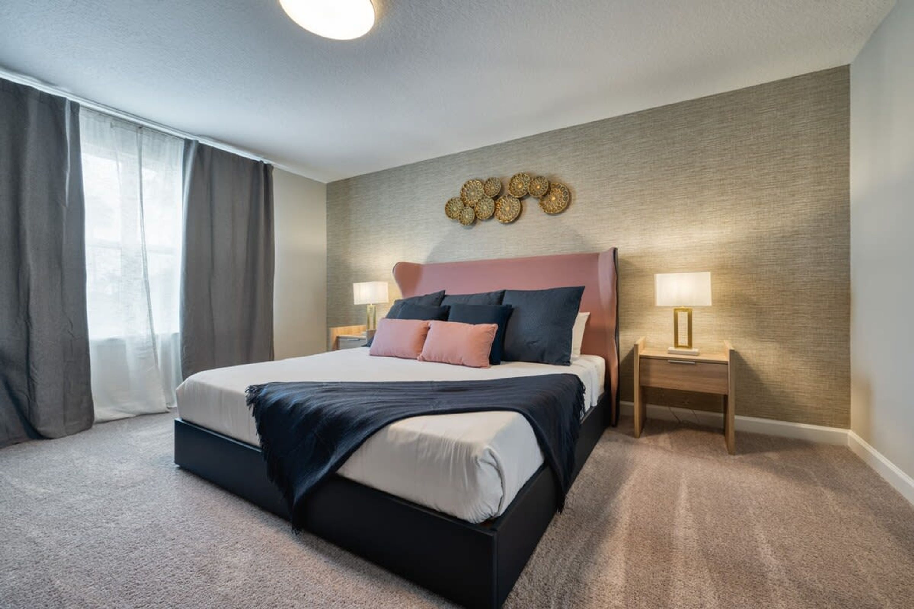 Ein Hotelzimmer mit einem großen Bett, zwei Nachttischen, einer Wandleuchte und einem Fenster mit Vorhängen.