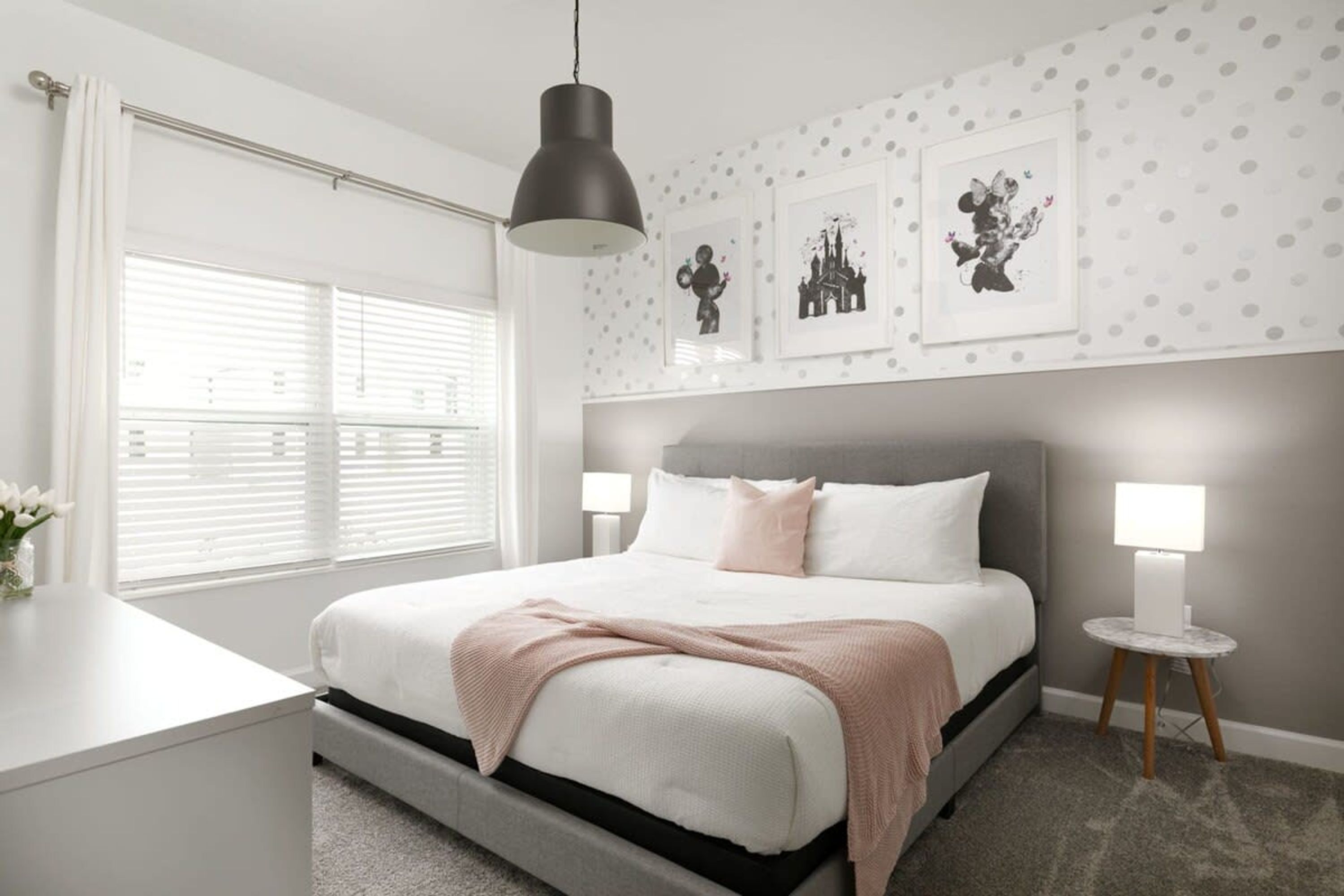 A modern bedroom with a large bed, bedside lamps, and a window with blinds.