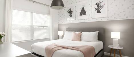 A modern bedroom with a large bed, bedside lamps, and a window with blinds.